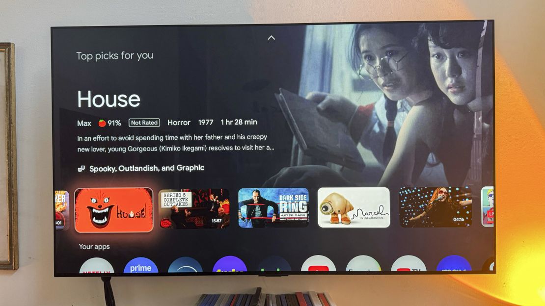 On a TV you see the horror movie "House" is a "Top Pick For You" on a TV connected to the (not shown) Google TV Streamer