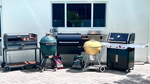 A group of grills on a stone patio including Nuke Delta, Big Green Egg, Traeger Ironwood 885, YAK Hibachi, Weber Ultimate Original Kettle, Weber Genesis E325s