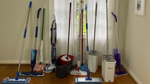 Group of string, pad, spin, and spray mops against a window in the corner of a living room.