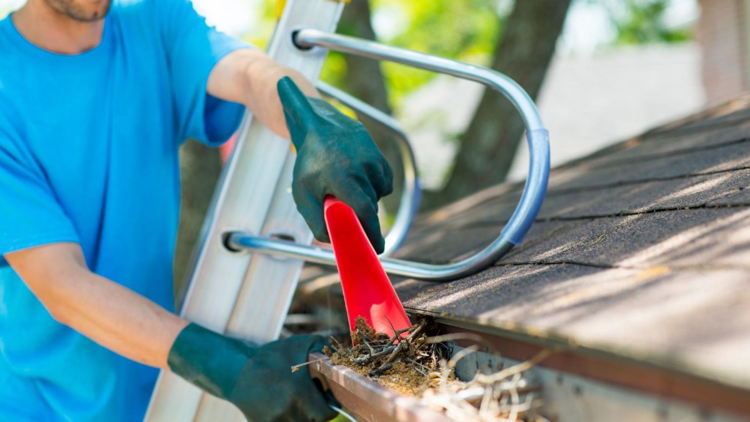 Professional gutter cleaner scoops leaves and sticks from a gutter.