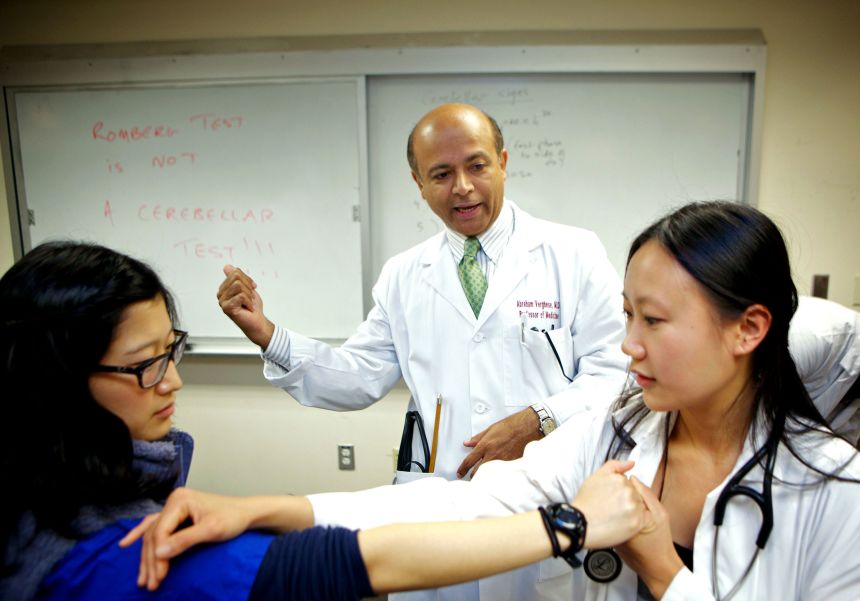 Abraham Verghese, center, watches as Dr Irene Sonu, left, and Vinca Chow, right, practice a physical technique for helping to diagnose various cerebellar disorders, in Palo Alto, California on August 27, 2010.