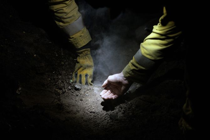 Firefighter Tristan Rios uses his bare hand to gauge the temperature of the ground while extinguishing hot spots in the Fernwood area of Topanga on Monday, January 13.