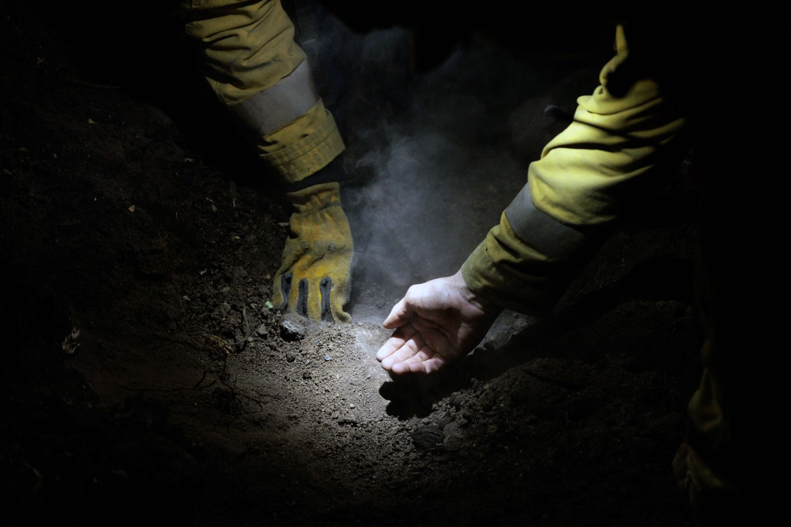 Firefighter Tristan Rios uses his bare hand to gauge the temperature of the ground while extinguishing hot spots in the Fernwood area of Topanga on January 13.