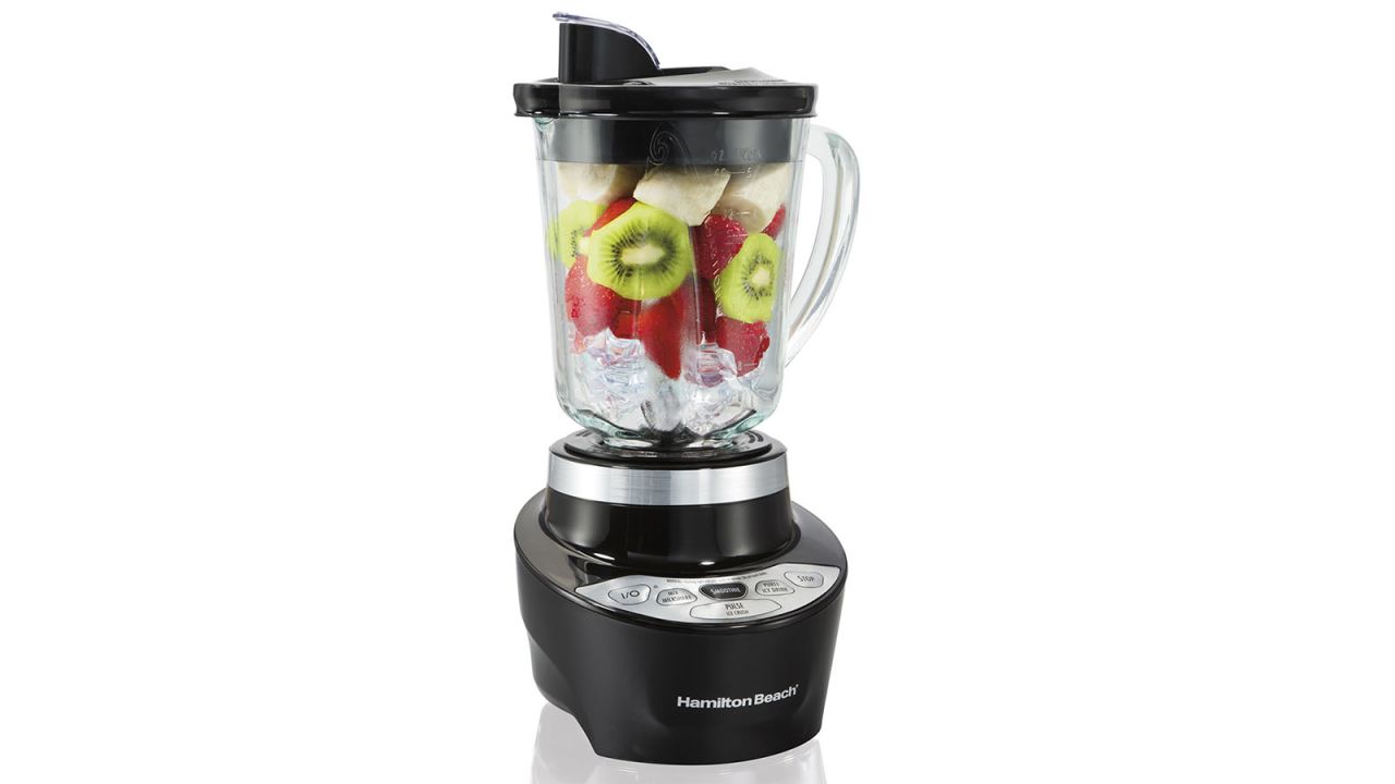 Blender with fruit and ice in it, placed against white background.