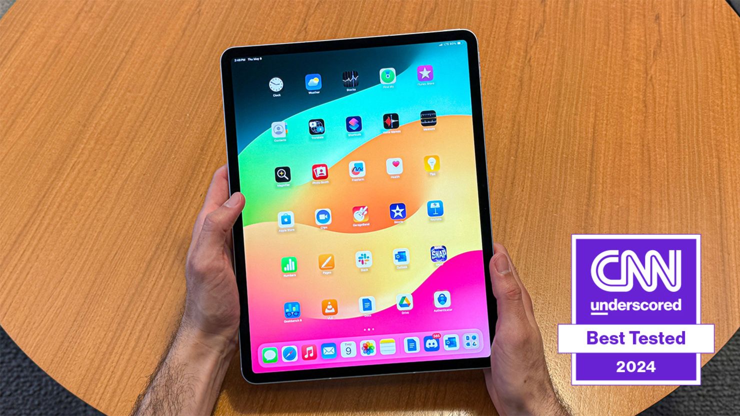 The iPad Air held in hands above a table, open to the icons on the home screen