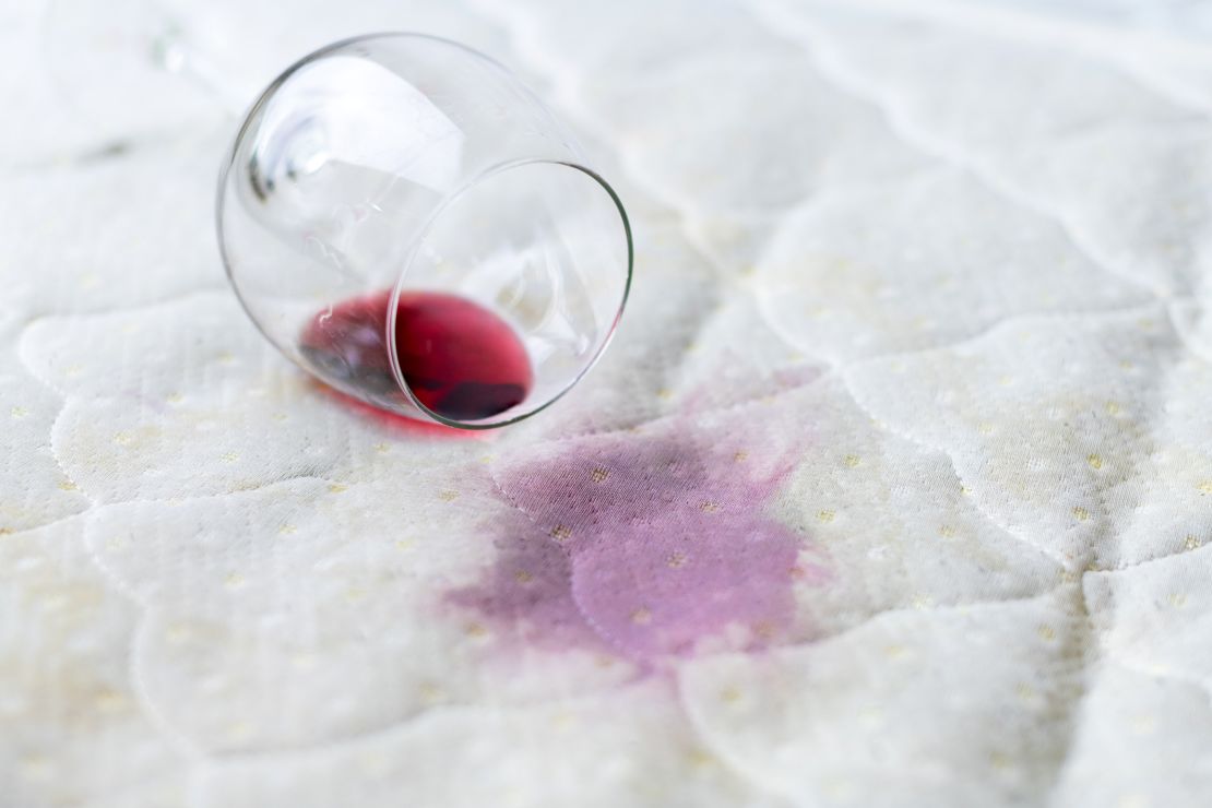 Spilled wine glass on the bed. Accidentally dropped wineglass on white bedsheet. Unlucky, unfortunate situation. Wet stain.