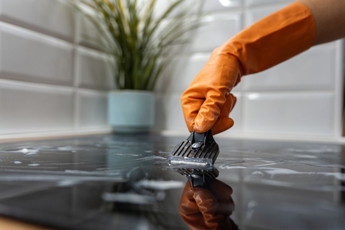 Close-up of an unrecognizable mid-adult Caucasian woman cleaning the glass-ceramic stove top, while scarping the dirt from it