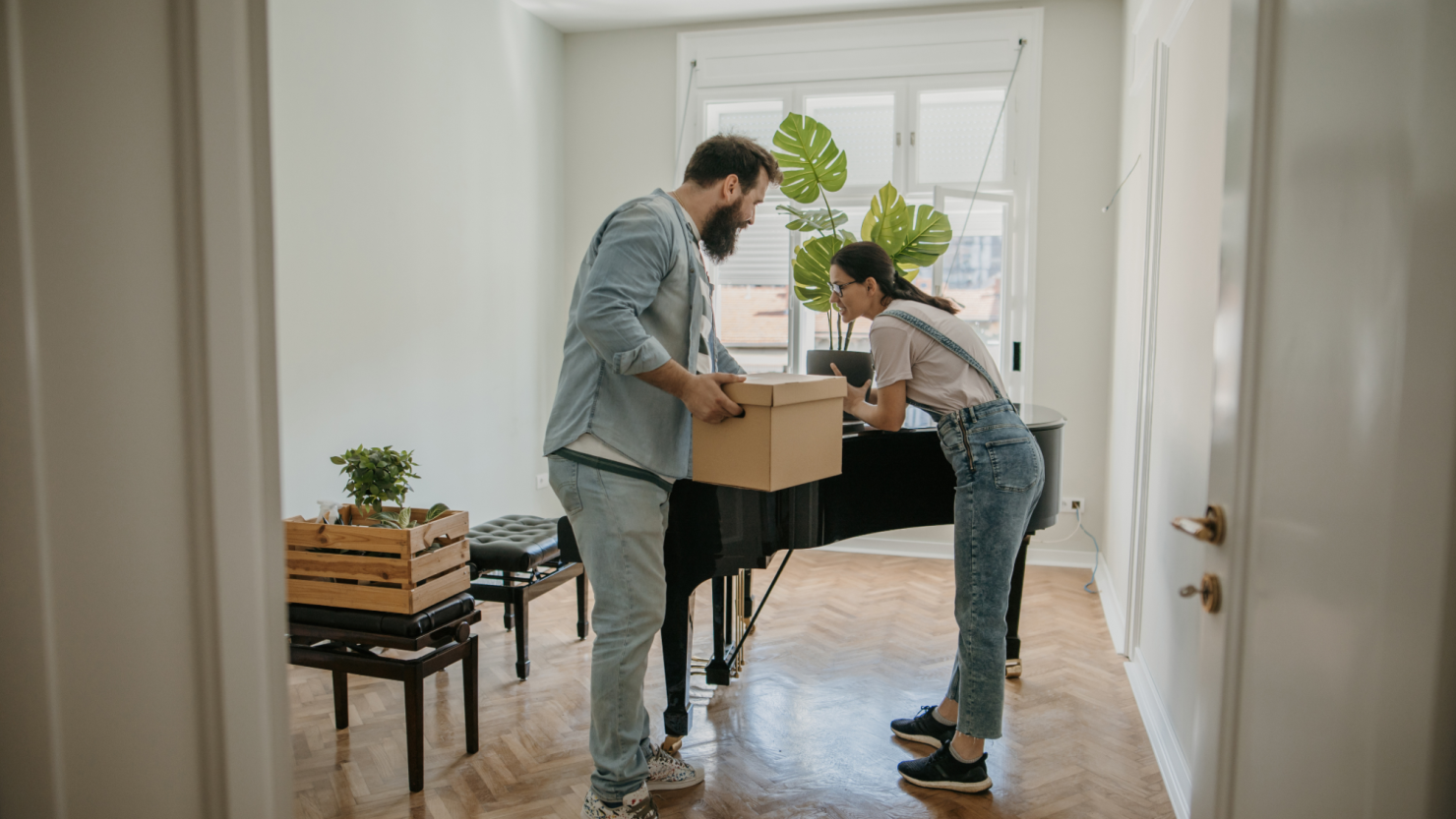 Couple moving boxes near a piano