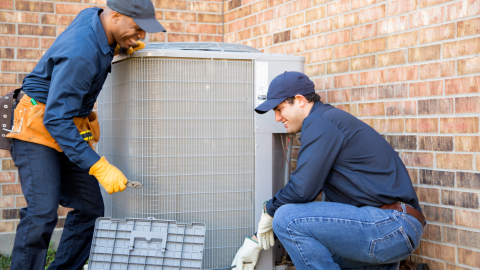 Two workers install an air conditioning unit.