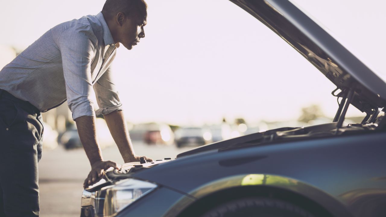 A photo of a person analyzing their car after breakdown on the street with the hood open.