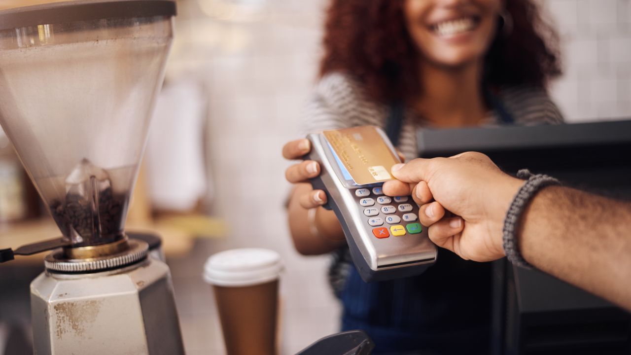 A photo of a person's hand tapping a credit card on a point of sale device at a coffee shop.