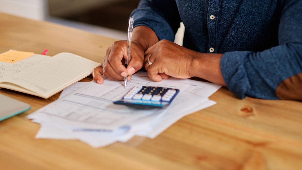 A photo of a person writing on a piece of paper while looking at a calculator