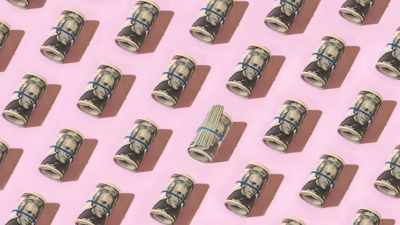 Rolls of $20 bills on a pink background.