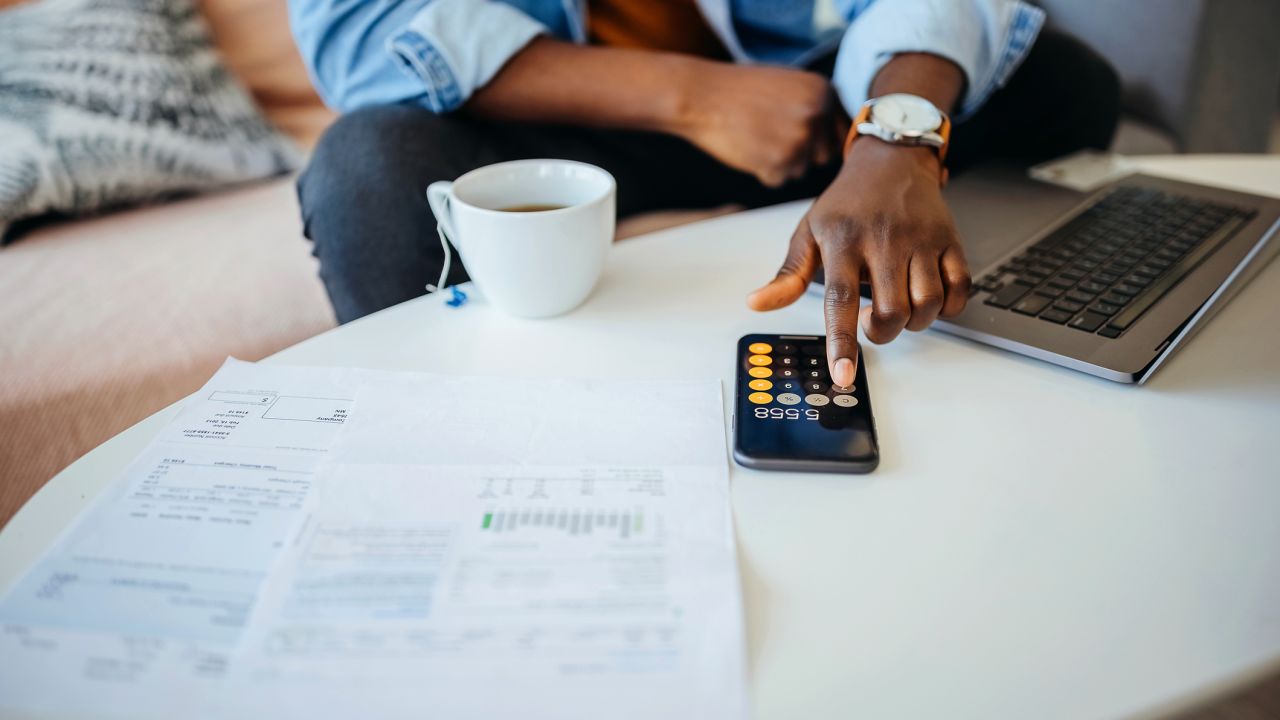 A photo of a person looking over finances while typing numbers into a cell phone calculator app.