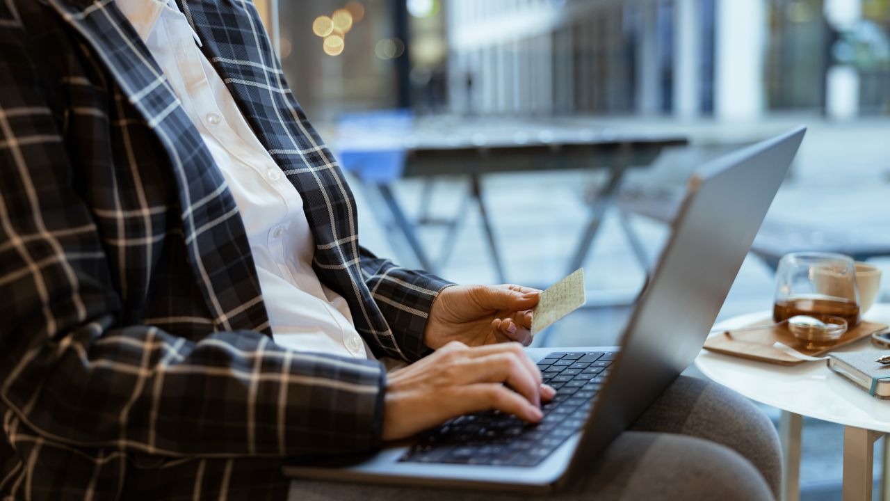 A photo of a person looking at a laptop and holding a credit card.