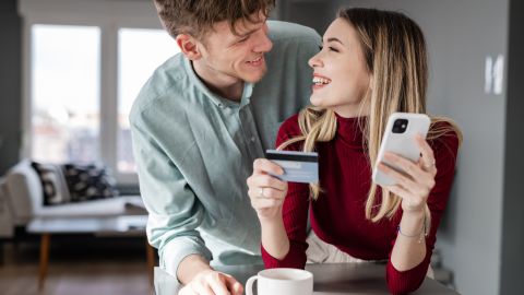 A couple looking at a phone and a credit card at home