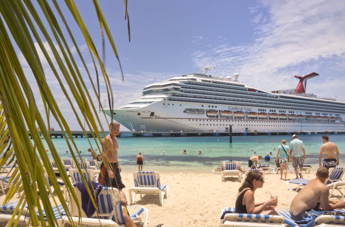 A photo of beachgoers relaxing on a beach overlooking a Carnival cruise ship