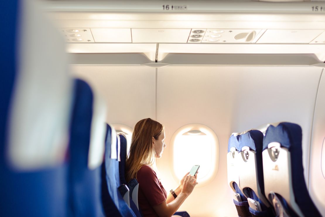 A photo of a person sitting in an airplane looking at a smartphone