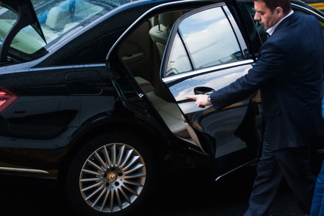 A photo of a driver opening the back door of a black Mercedes-Benz sedan in London