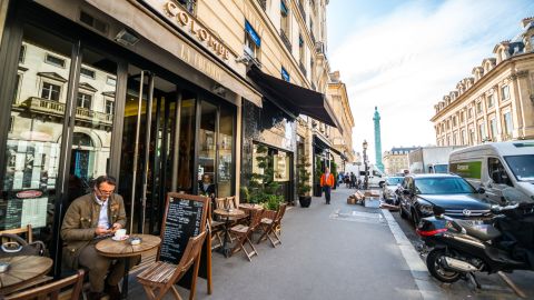 A wide photo of a person drinking coffee and looking at a cell phone at a cafe in Paris