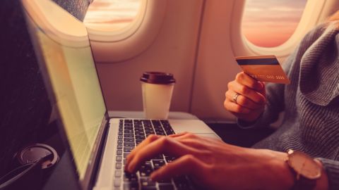 A photo of a person typing a credit card number into a laptop on an airplane