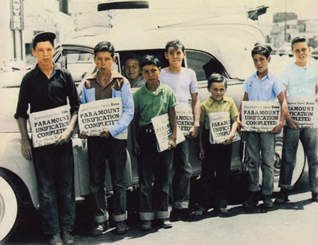 Chicos repartidores con periódicos titulados "Paramount Unification Completed" ("Completada la Unificación de Paramount") en 1948.