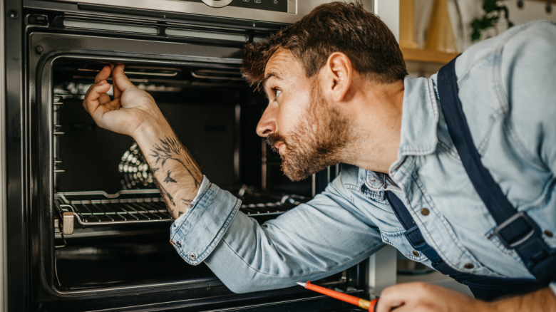 Handyman repairs oven in customer’s kitchen.