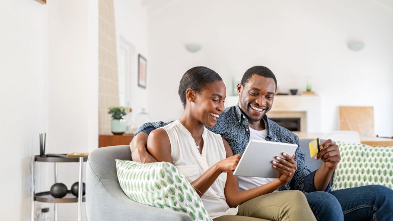 Couple sitting on their couch while using the internet on their tablet.