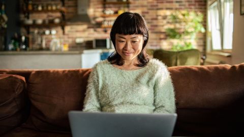 Person sitting on their couch while working on a computer.