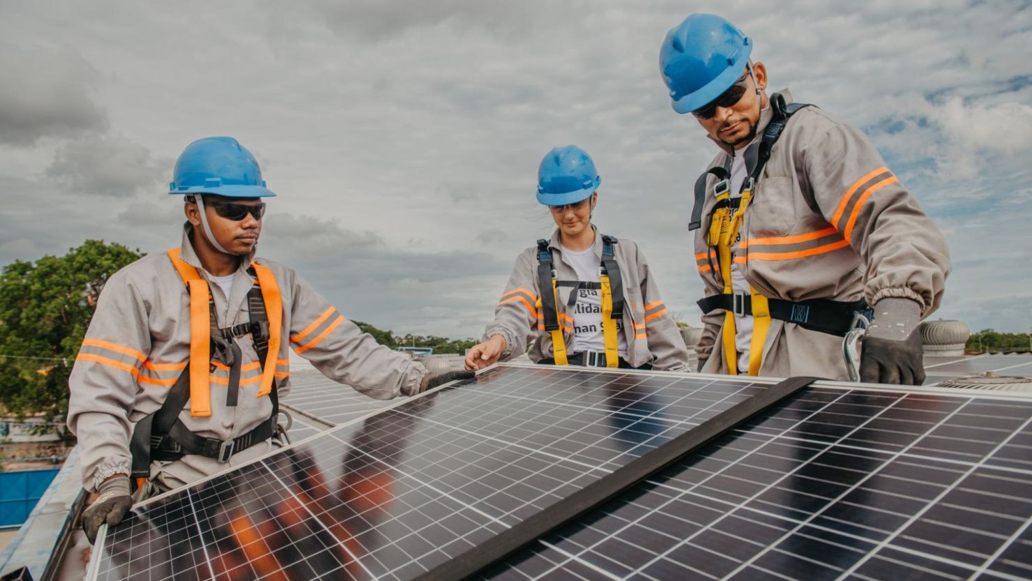 Three solar panel technicians install solar panels on the roof of a home.