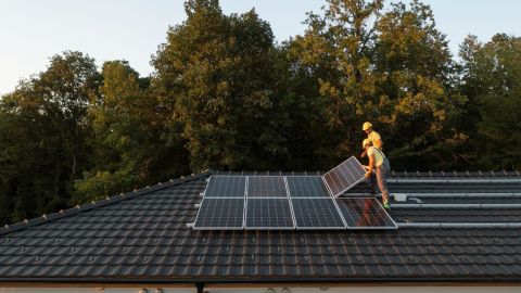 Workers install solar panels on a residential roof.