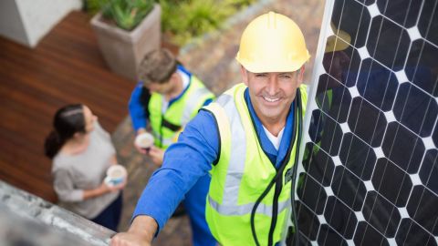  Solar panel installer carrying a solar panel up a ladder and onto the roof.