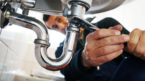 Service technician tightening a pipe under a sink.