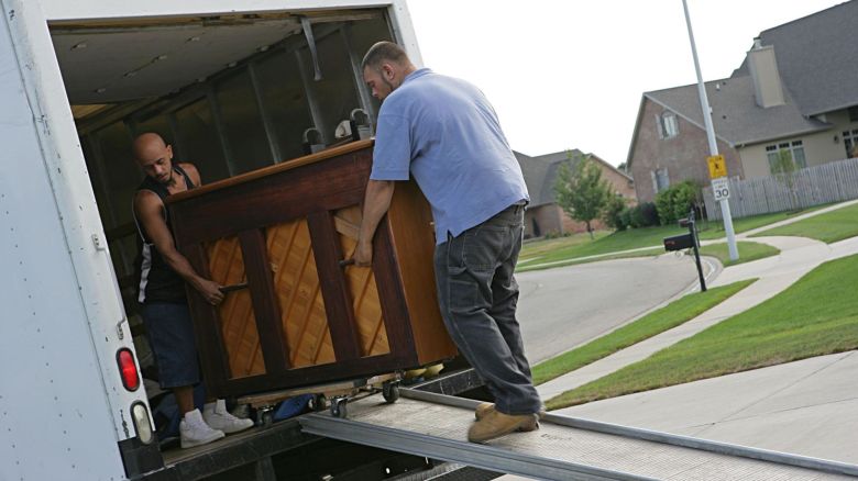 Two movers loading a piano into a truck.