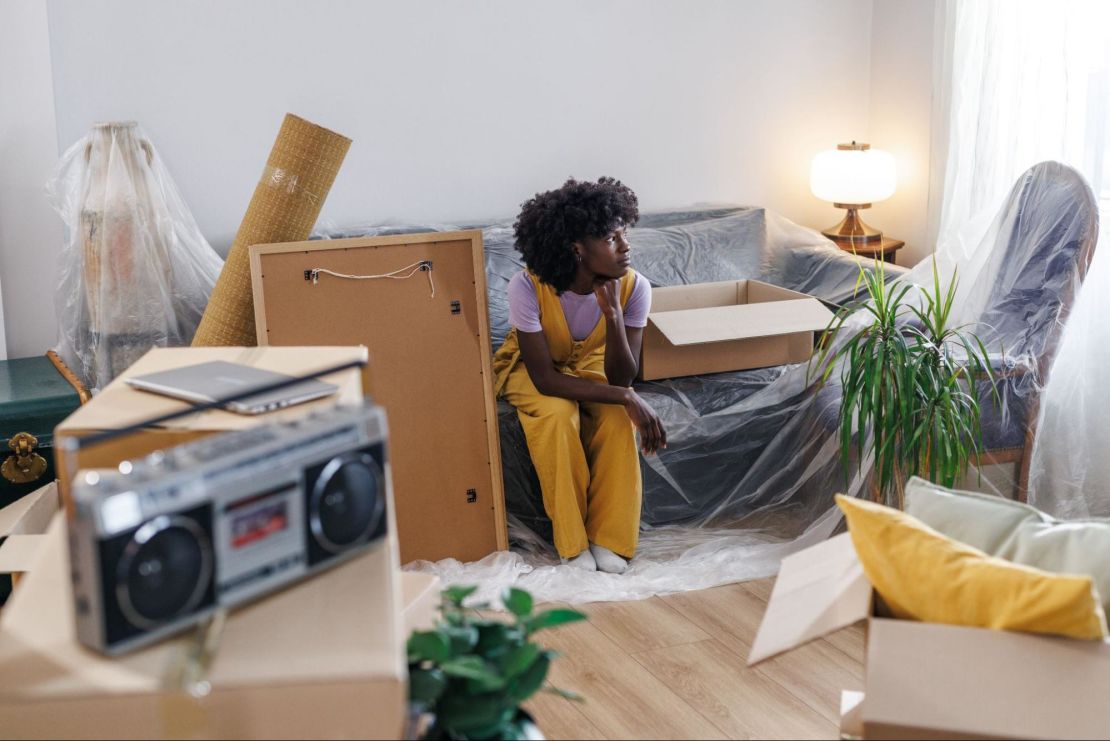 Person sitting in their living room full of moving boxes.