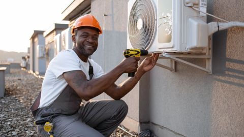 HVAC technician kneeling next to an HVAC unit.