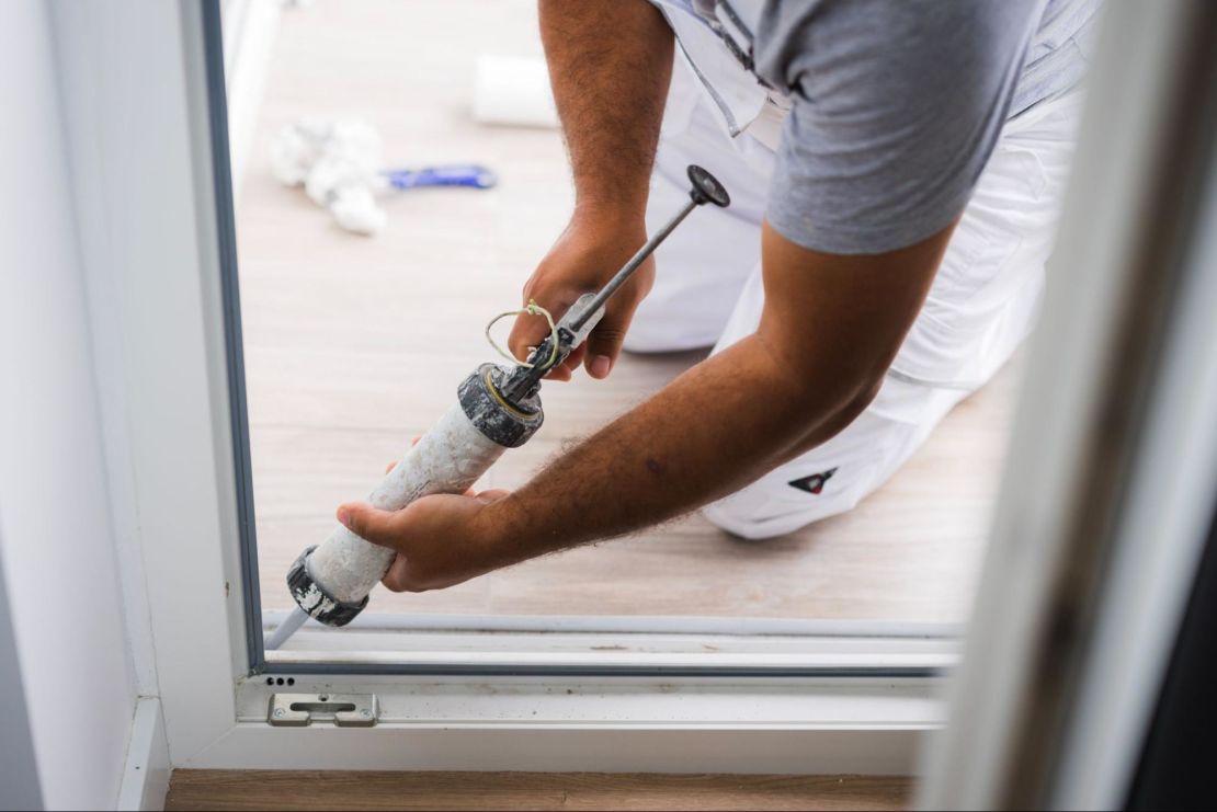 Window replacement specialist using a silicone gun on the back of a balcony door.