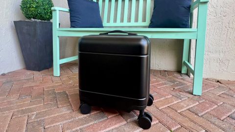 A photo of a black Calpak Hue Mini suitcase in front of a teal bench on a residential outdoor patio