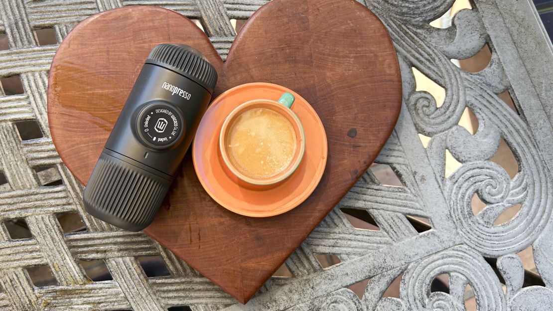 Nanopresso next to cup of espresso on a wooden cutting board.