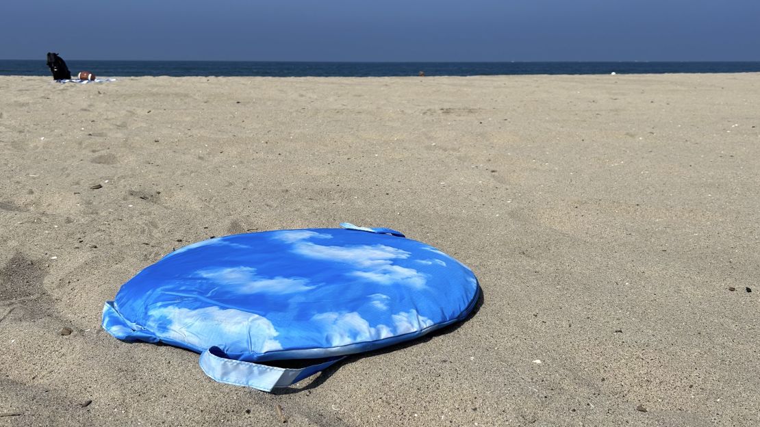 Baggu Pop Up Tent in circular case placed on the sand, ocean in the horizon.