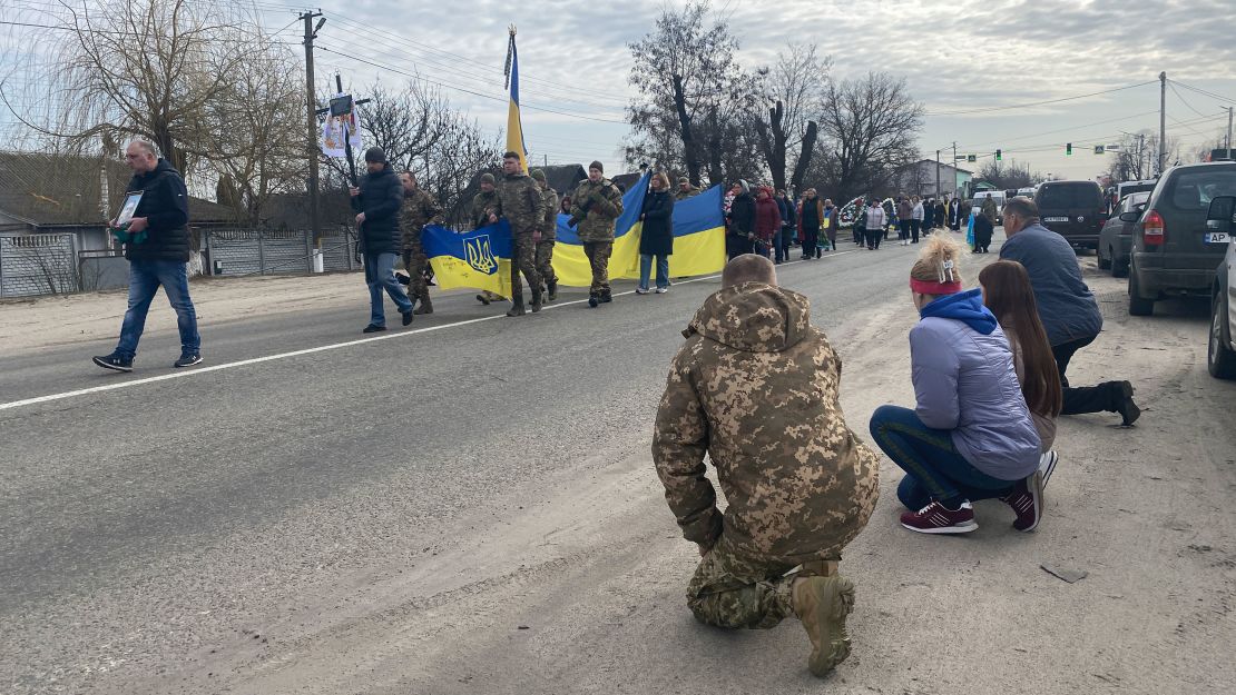 People kneel as they line the main road in the village of Demydiv, just north of Kyiv, while the funeral procession for Oleksandr Savchenko passes by.