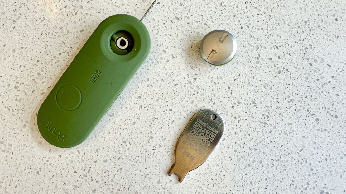 A green Knog Scout Luggage Tag with its included installation key