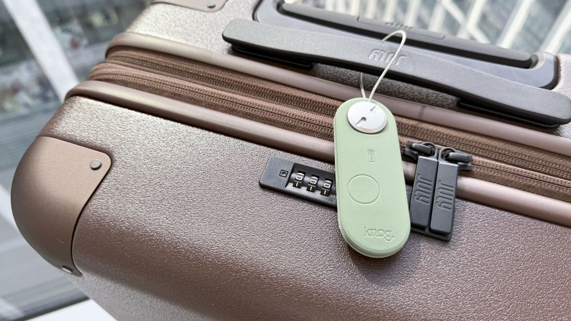 A light green Knog Scout Luggage Tag attached to a brown July suitcase