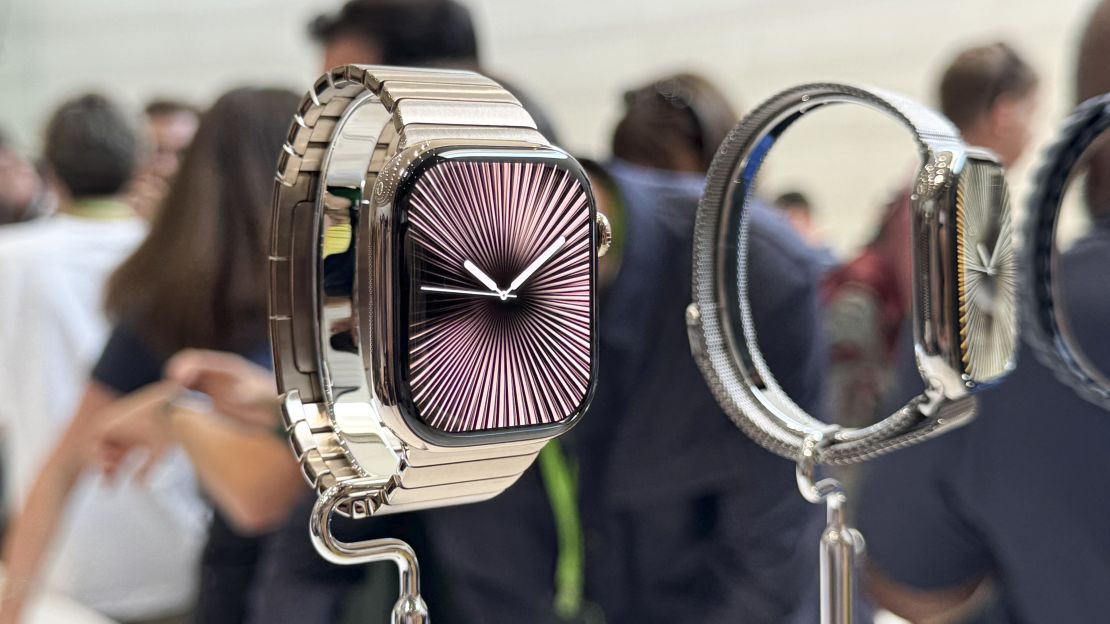 A metallic Apple Watch Series 10 on a stand on a crowded show floor