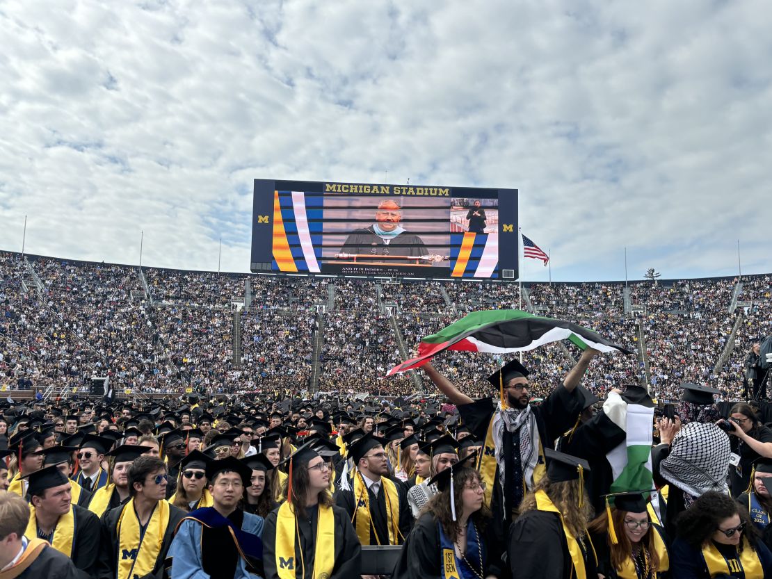 A protester holds a Palestinian flag as the Secretary of the Navy delivered remarks at the University of Michigan’s 2024 spring commencement.
