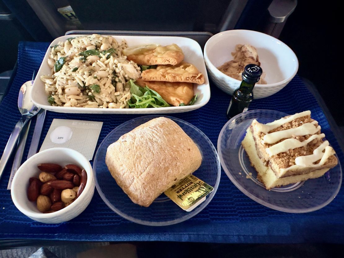 A photo of a United domestic first class meal with an entree, bread roll, nuts and cake