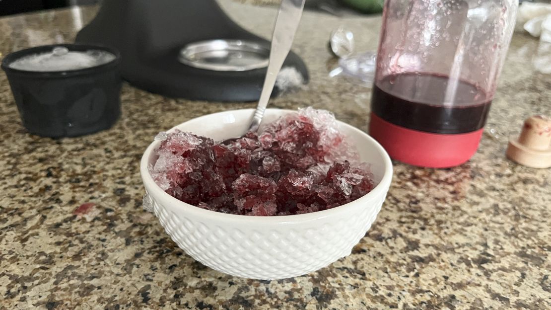 A small bowl of shaved ice doused in cherry syrup on a kitchen counter.