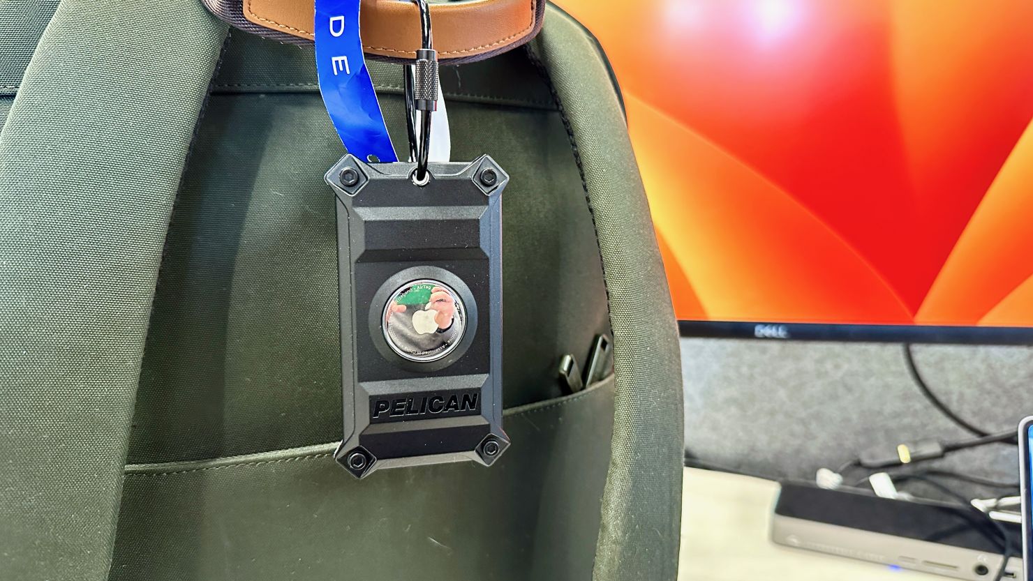 A photo of the Pelican Luggage Tag for AirTags attached to a green backpack