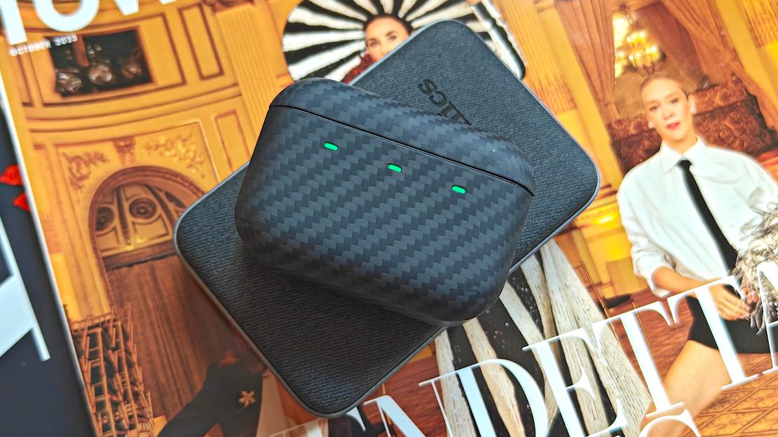 An earbuds case and a portable charger stacked on a magazine.