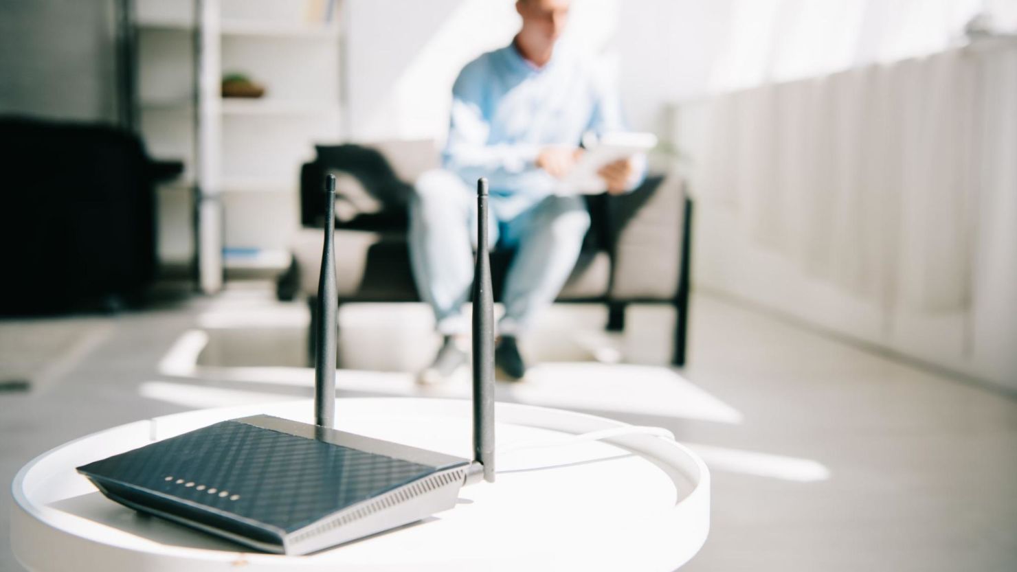 Close-up of a router with a man sitting on the couch in the background.